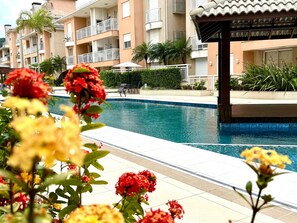 A swimming pool with a tiled deck, surrounded by multi-story buildings with balconies. - Residencial com piscina (Florianópolis)