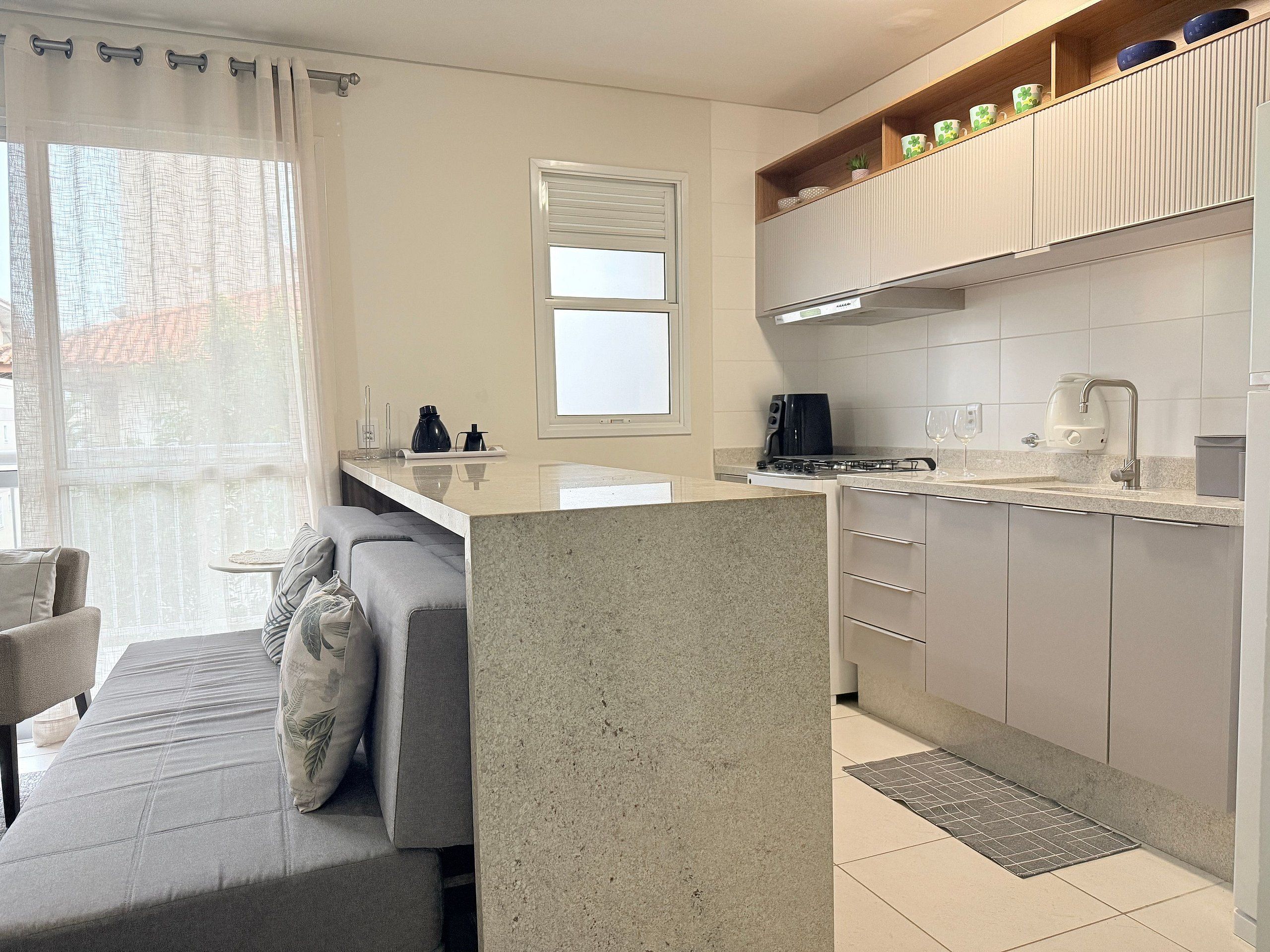 Una cocina moderna con una isla central, un comedor con sofá y un ventanal con cortinas.
