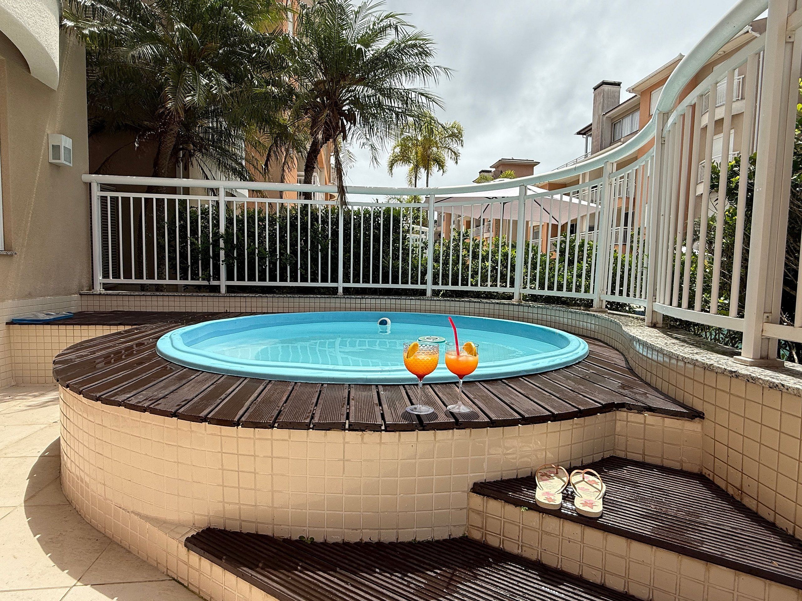 An outdoor swimming pool with a wooden deck, surrounded by a white fence and palm trees.