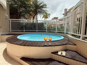 An outdoor swimming pool with a wooden deck, surrounded by a white fence and palm trees.