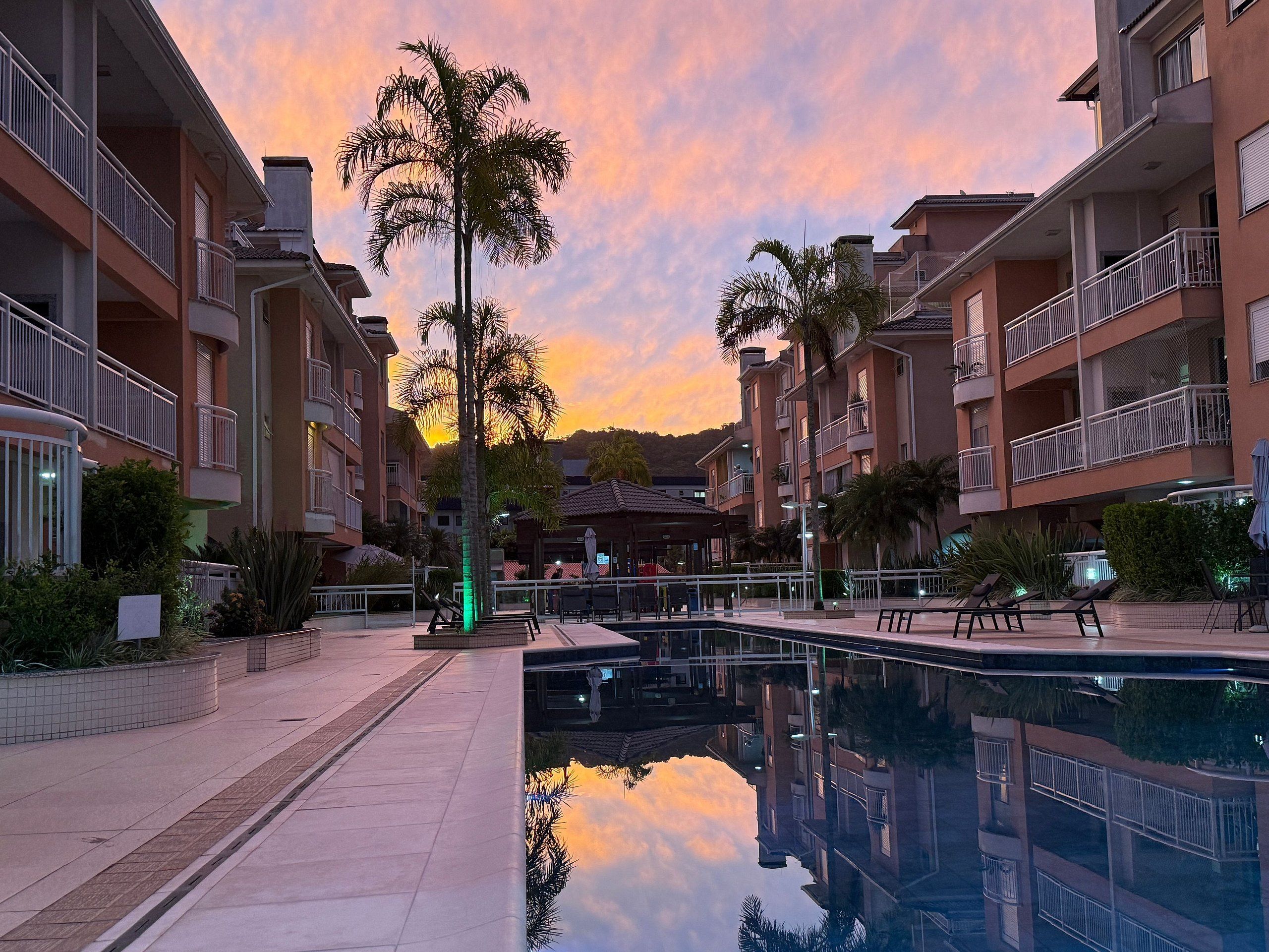 A residential building with balconies, a swimming pool, and palm trees.