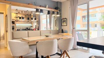 A modern dining area with a glass-top table, four chairs with wooden legs, and pendant lighting.