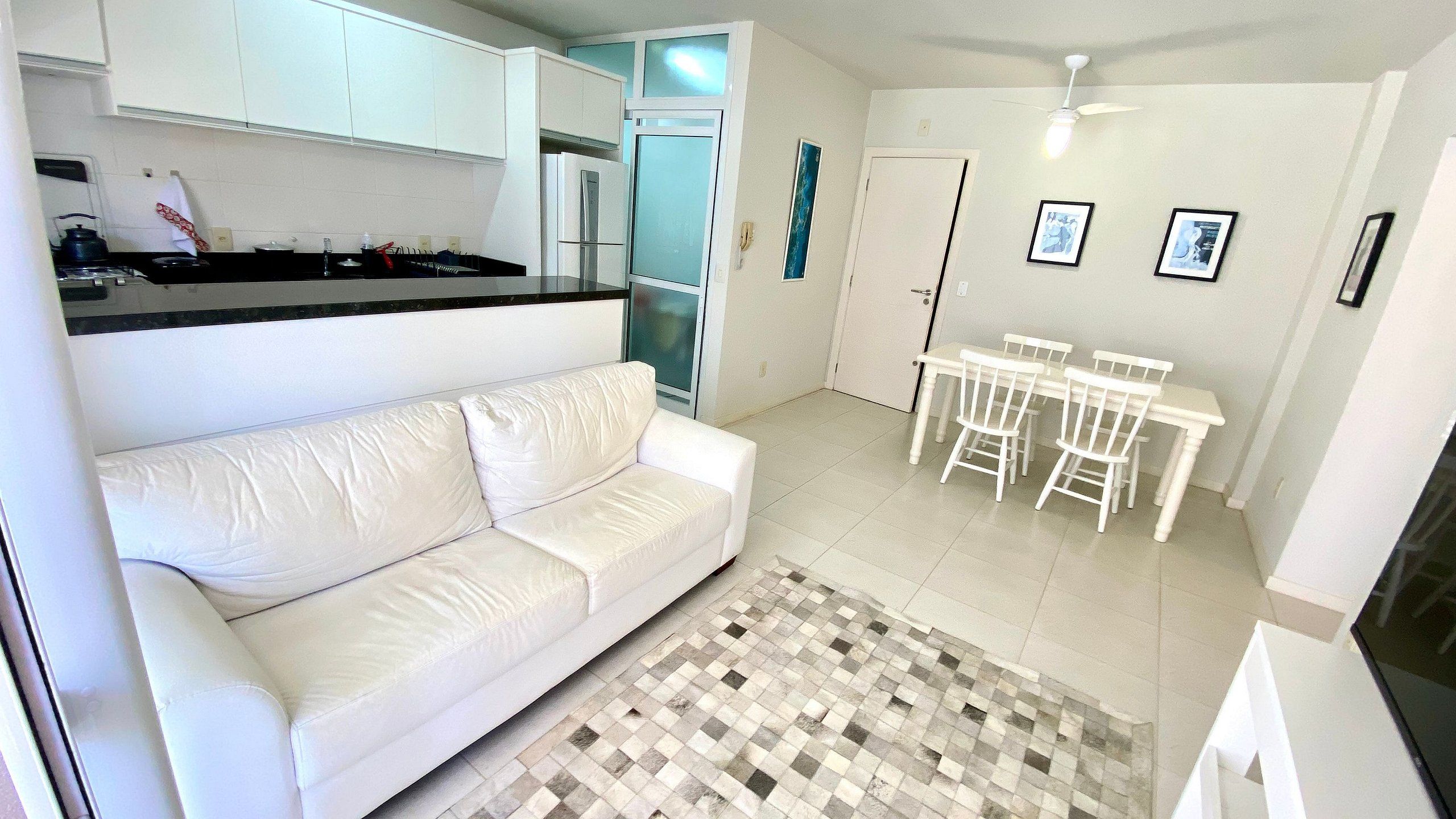 Un espacio habitable pequeño con kitchenette, un sofá blanco, una mesa de comedor con sillas y una alfombra estampada.