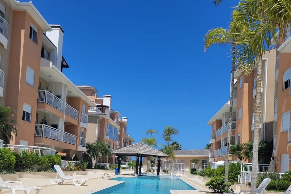 A swimming pool with lounge chairs, a covered seating area, and multi-story buildings with balconies.