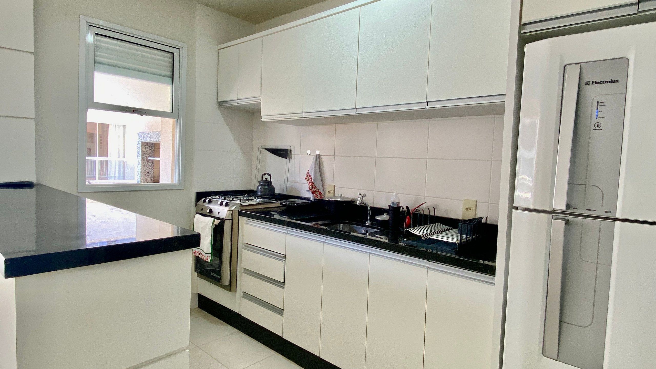 Una cocina con armarios blancos, una estufa, un fregadero y un refrigerador.