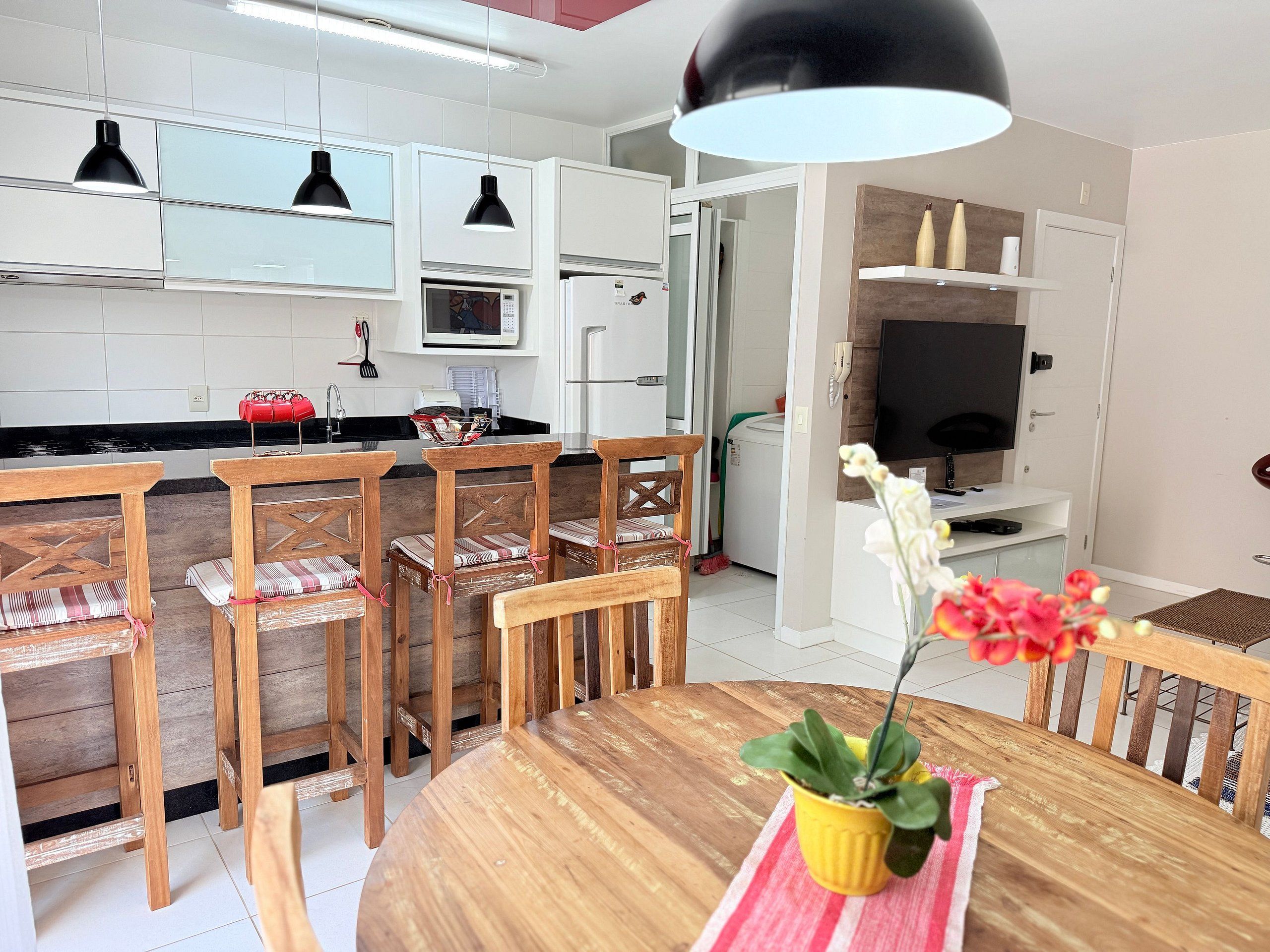 Une cuisine moderne avec des meubles blancs, un four à micro-ondes et un réfrigérateur. On y trouve également un coin repas avec des chaises et une table en bois.