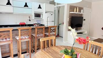 Une cuisine moderne avec des meubles blancs, un four à micro-ondes et un réfrigérateur. On y trouve également un coin repas avec des chaises et une table en bois.