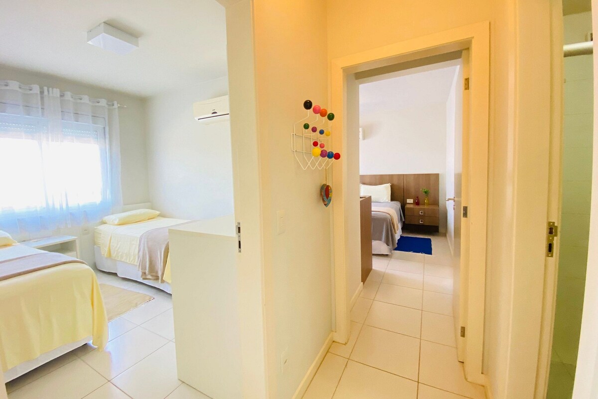 A hotel room with two beds, a bathroom, and a hallway leading to another room.