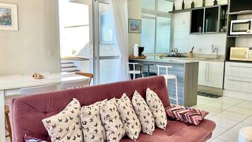 Una sala de estar con un sofá, una mesa de comedor y una cocina con microondas y armarios.