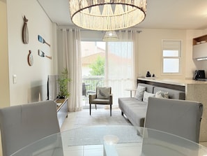 Una sala de estar moderna con sofá, sillas, mesa de comedor, televisor, planta y vistas al exterior.
