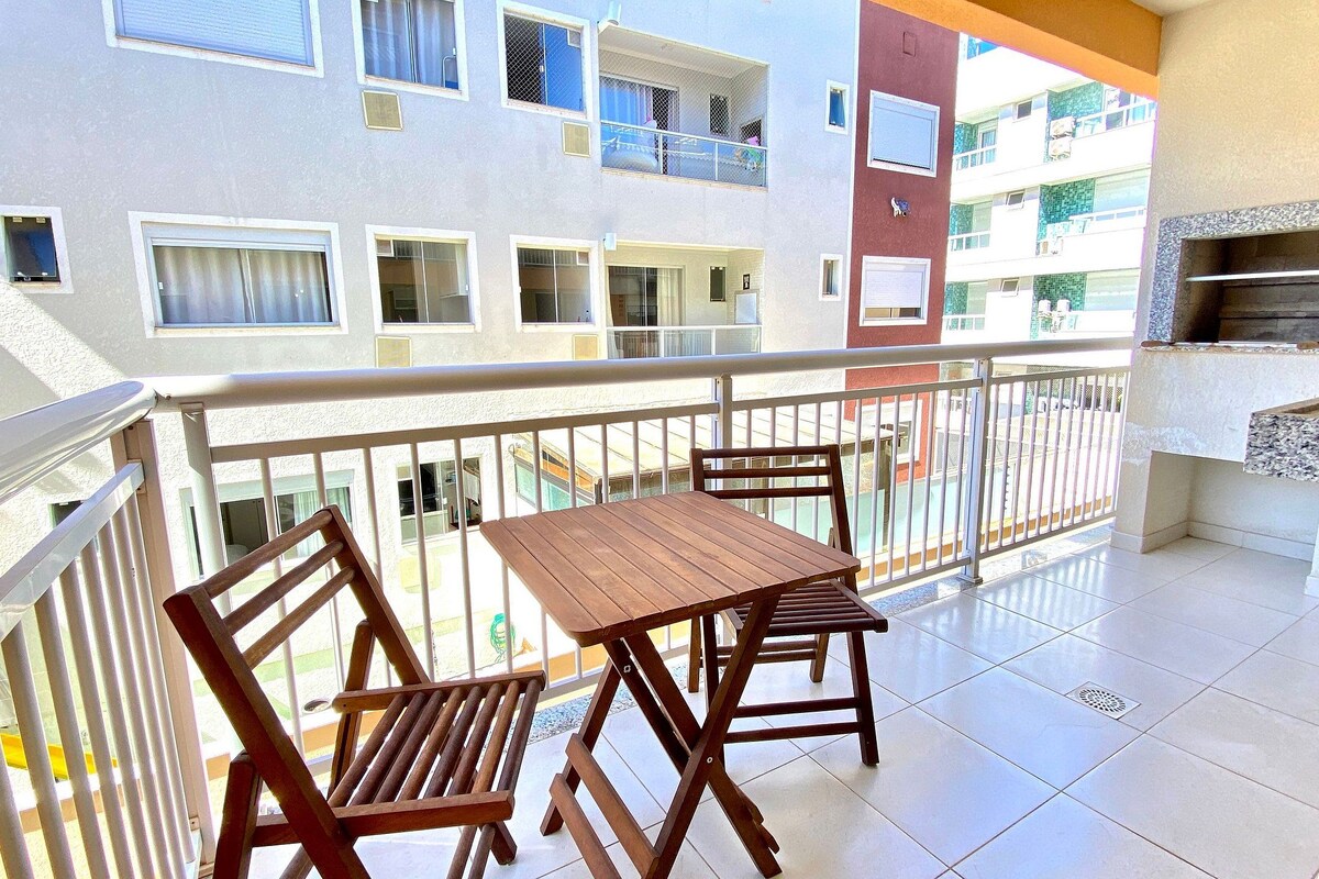 A balcony with a wooden table and chairs, a small kitchen area with a countertop, and a view of neighboring buildings.
