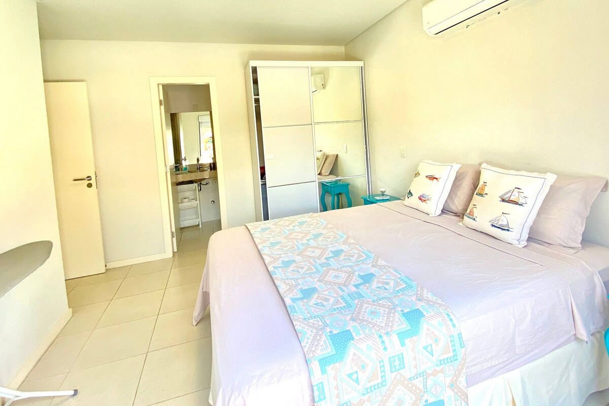 A bedroom with a bed, a desk, a chair, a mirror, and a bathroom visible through an open door.