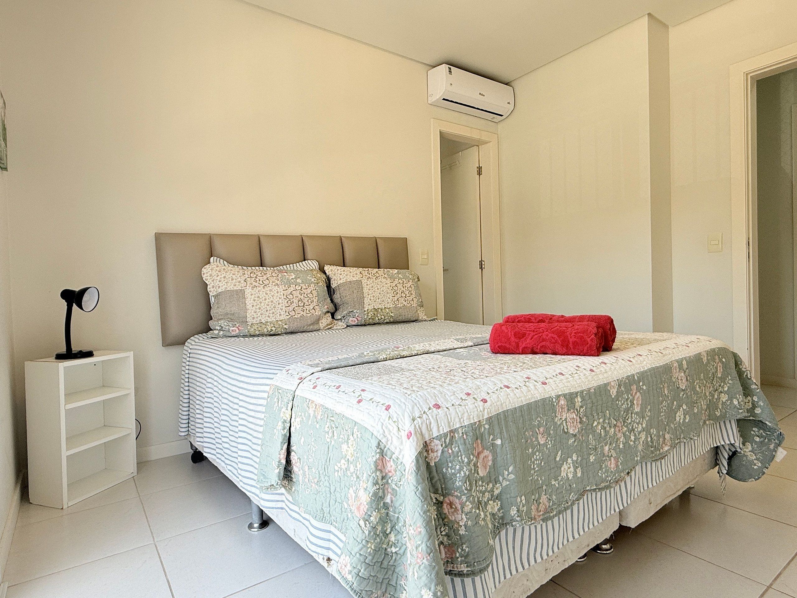 Een slaapkamer met een bed, een nachtkastje, een rode deken en een airconditioning.