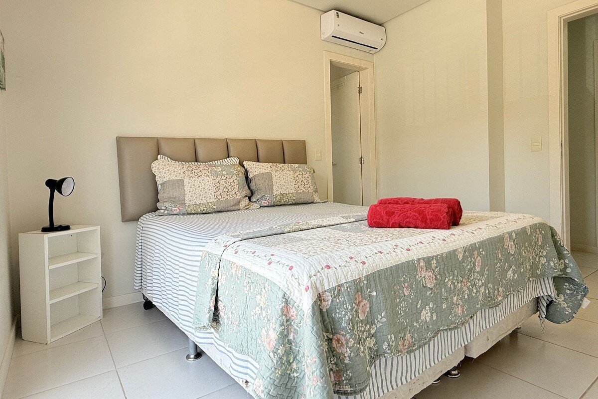 A bedroom with a bed, a nightstand, a red blanket, and an air conditioning unit.
