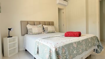 Een slaapkamer met een bed, een nachtkastje, een rode deken en een airconditioning.