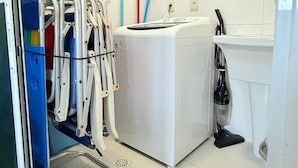 A laundry room with a washing machine, a drying machine, a cart with cleaning supplies, and a vacuum cleaner.
