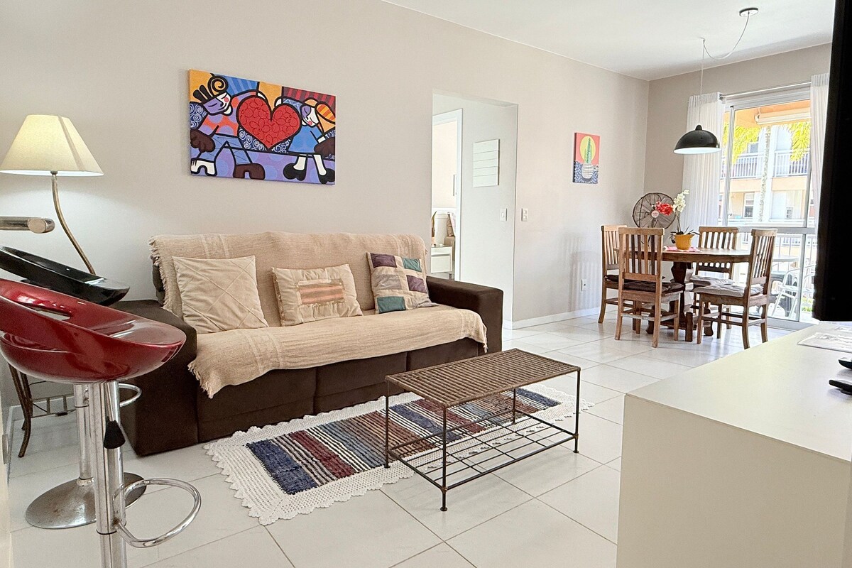 A living room with a sofa, a coffee table, a dining area with chairs, a lamp, and a painting on the wall.
