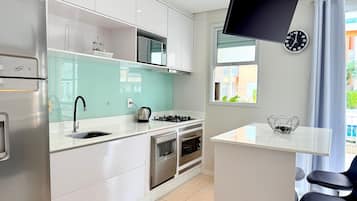 Une cuisine moderne avec des armoires blanches, un réfrigérateur en acier inoxydable, une cuisinière à gaz et un téléviseur à écran plat fixé au mur.