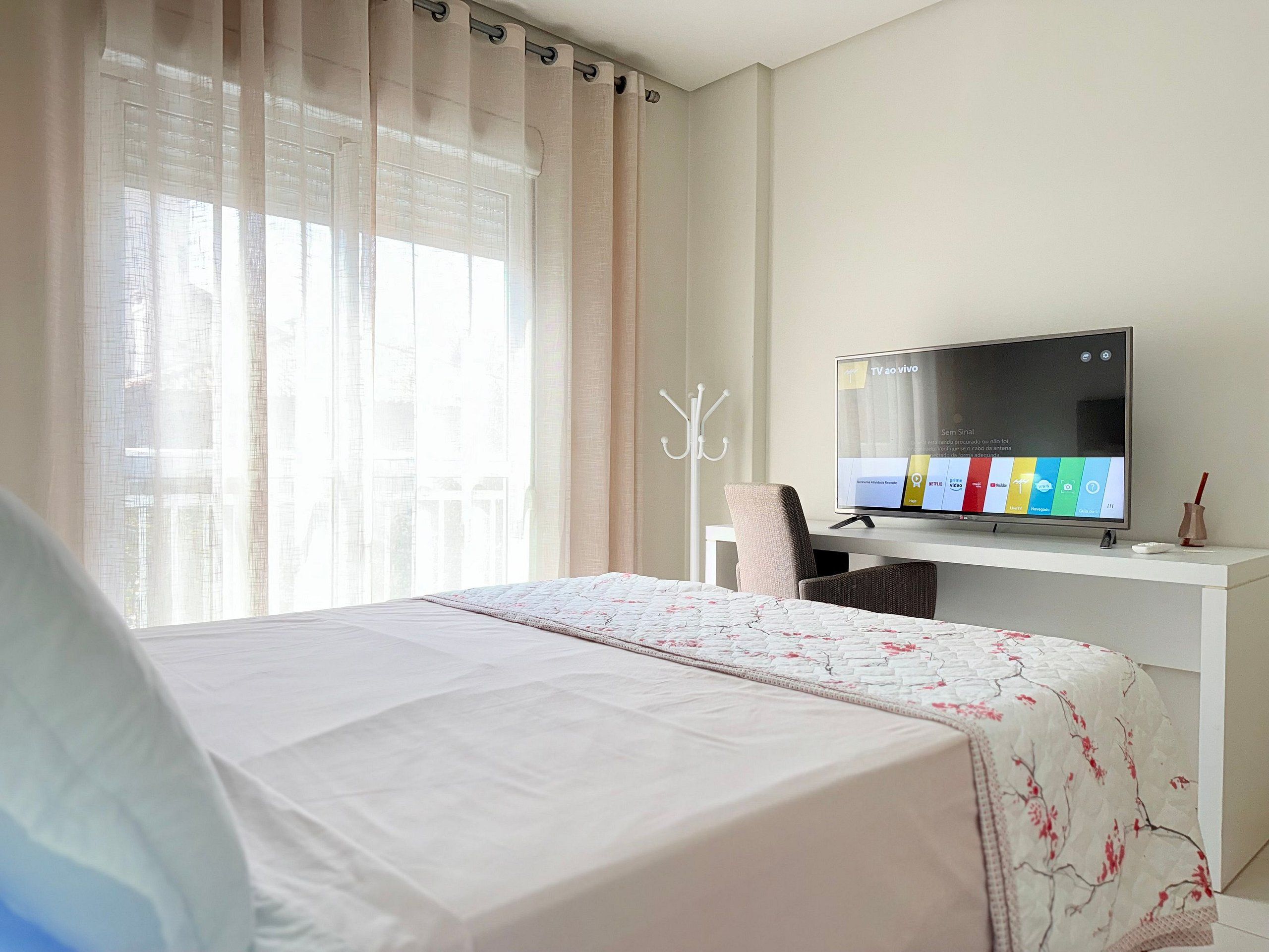 Una habitación de hotel con una cama, un televisor sobre un mueble, un escritorio y una ventana con cortinas.
