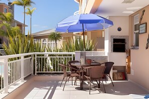 A balcony with a table and chairs, a blue umbrella, and a stone fireplace.