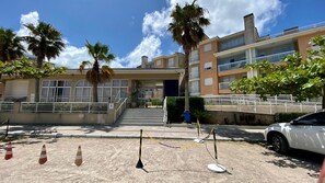 Entrada de un hotel con una escalera que lleva a la recepción, palmeras y un coche blanco estacionado cerca.