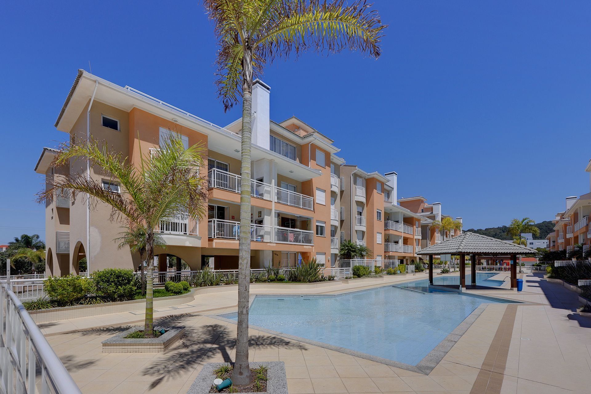 Un hotel de varios pisos con balcones, piscina y palmeras.