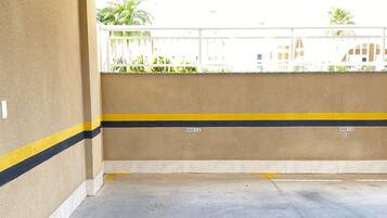 Un estacionamiento vacío con pisos y paredes de concreto, espacios de estacionamiento delimitados y vistas a edificios y áreas verdes en el exterior.
