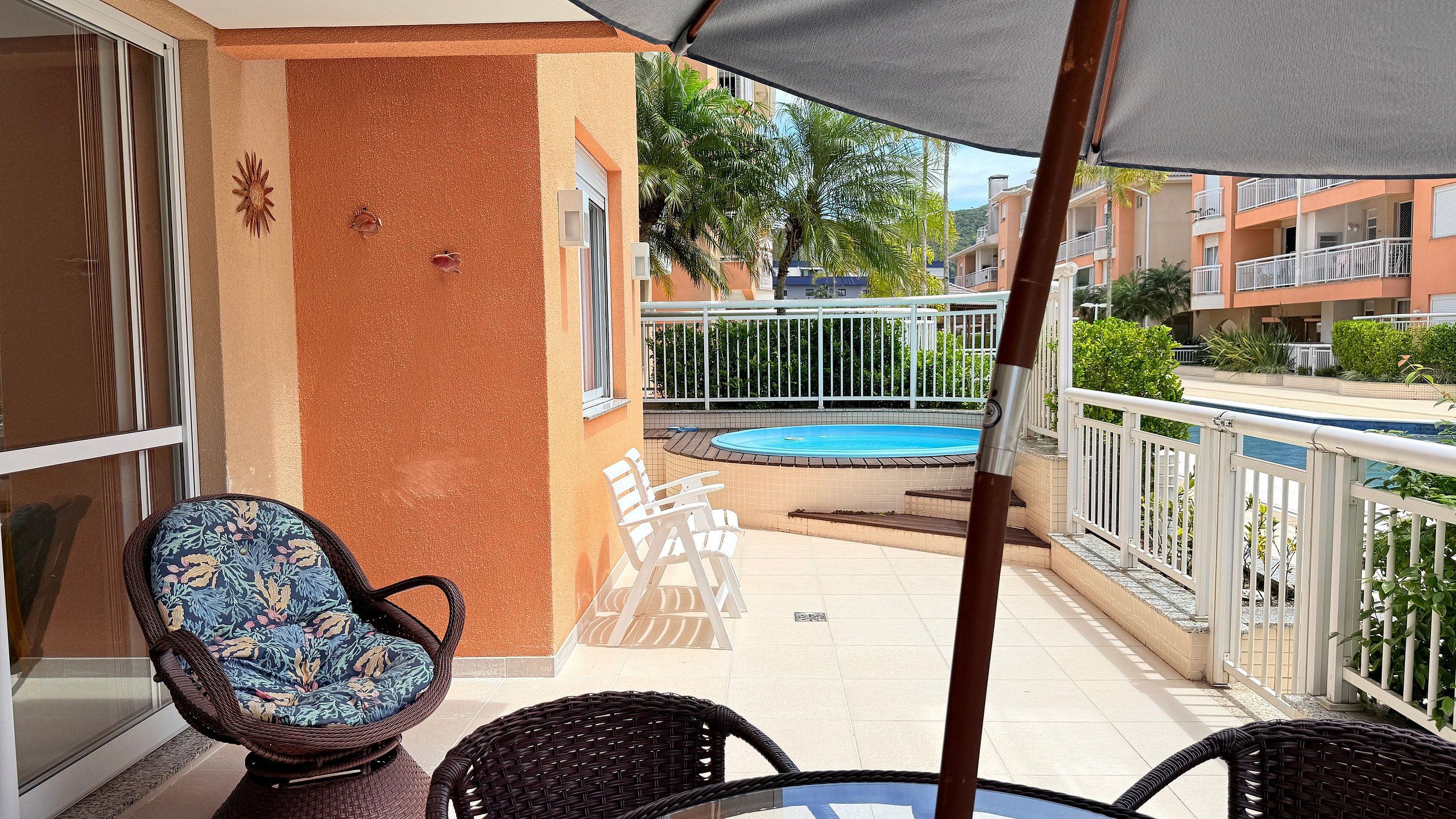 A balcony with a pool, wicker chairs, and a view of neighboring buildings.