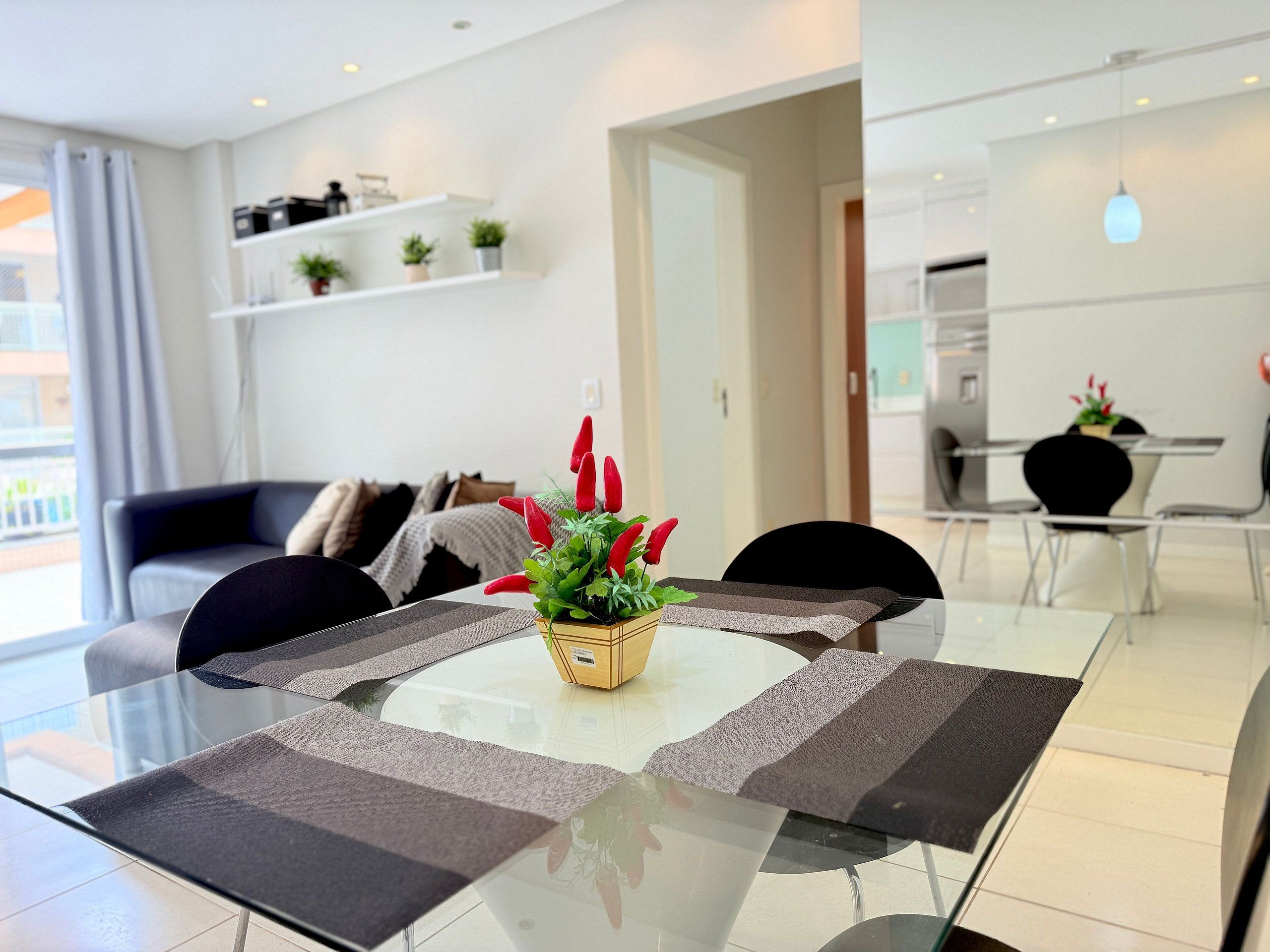 Un comedor moderno con una mesa de vidrio, individuales negros y grises, y un centro de mesa con flores rojas.