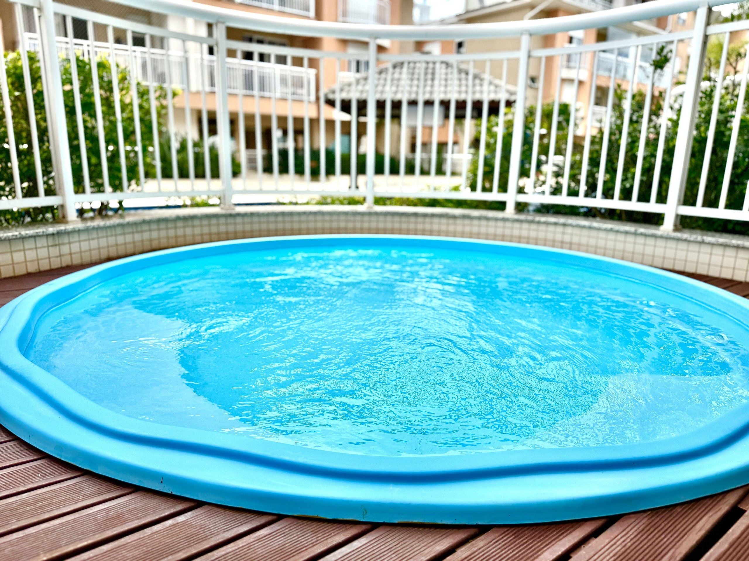 A round swimming pool with a blue edge, surrounded by a white fence, and a wooden deck.