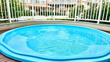 A round swimming pool with a blue edge, surrounded by a white fence, and a wooden deck.