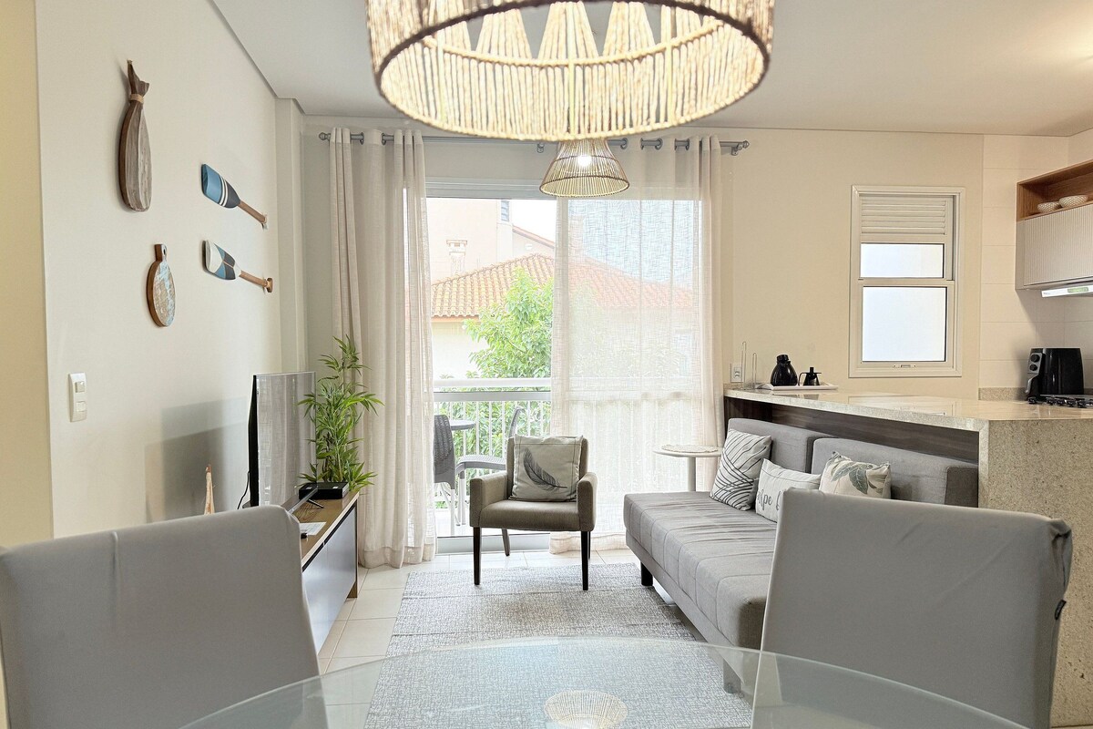 A modern living room with a sofa, chairs, a dining table, a TV, a plant, and a view of the outside.