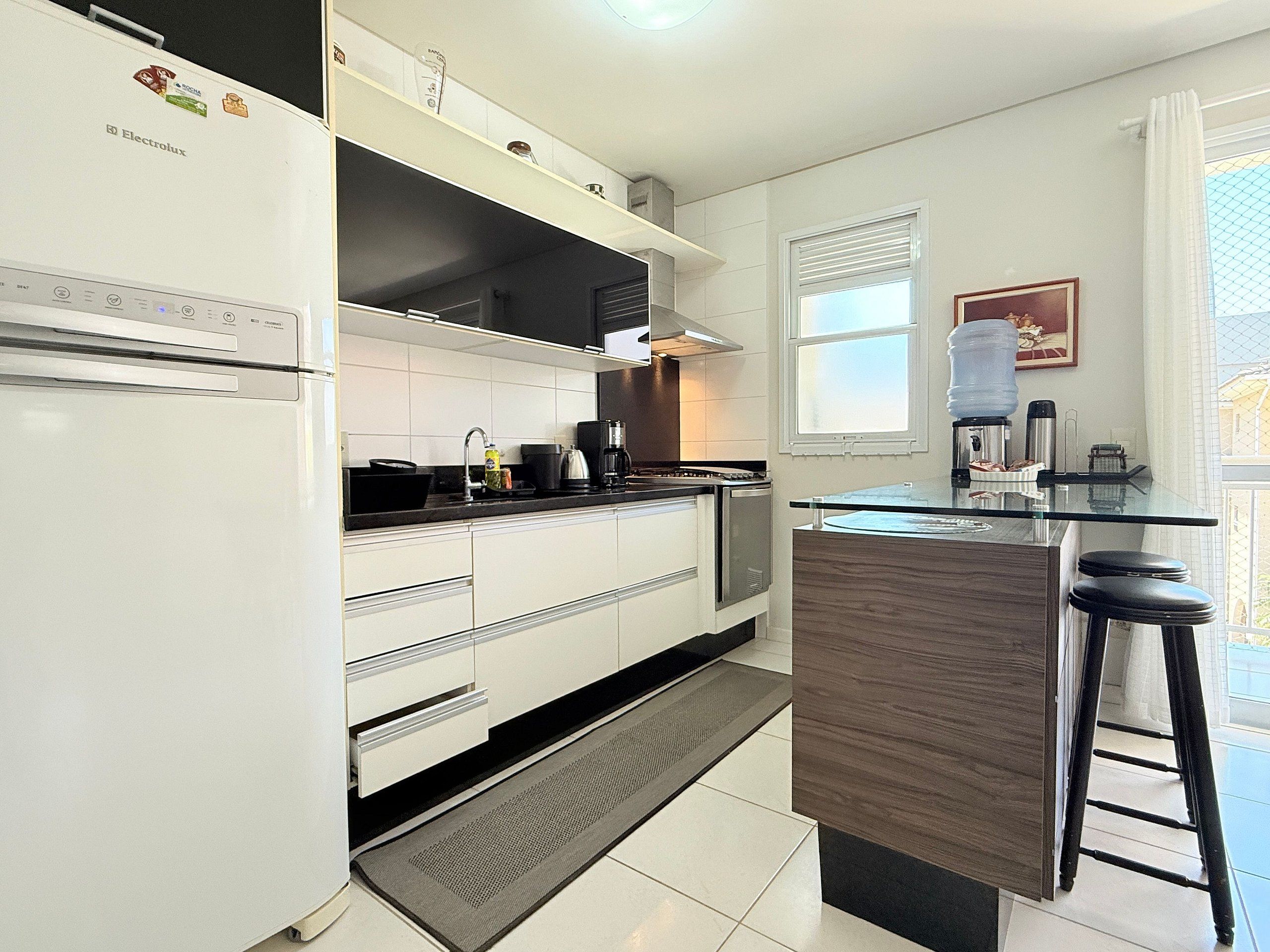 Una cocina moderna con armarios blancos, horno empotrado, cafetera y un taburete de bar.