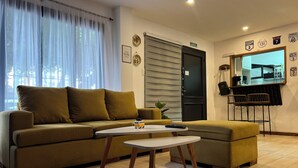 A living room with a sofa, a small table, a door, a mirror, and a kitchen area with a counter and chairs. - Allpa Andina Hostel (Mendoza)