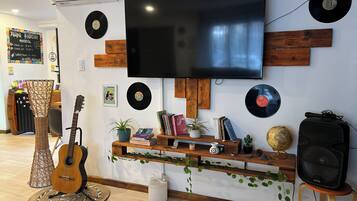 A room with a flat-screen TV, wooden shelves with books and decorative items, a guitar, a globe, and a speaker.