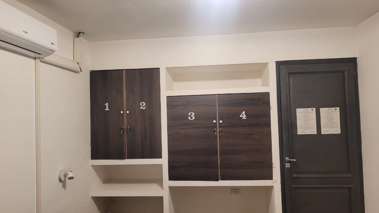 Quarto com armários de armazenamento numerados e uma porta com avisos.