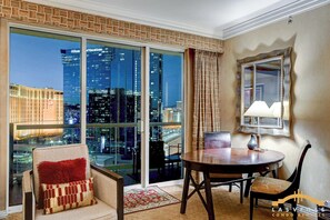 Ein Hotelzimmer mit einer großen Glasschiebetür, einem runden Esstisch, einem Stuhl, einer Couch mit rotem Kissen und einem Spiegel an der Wand.
