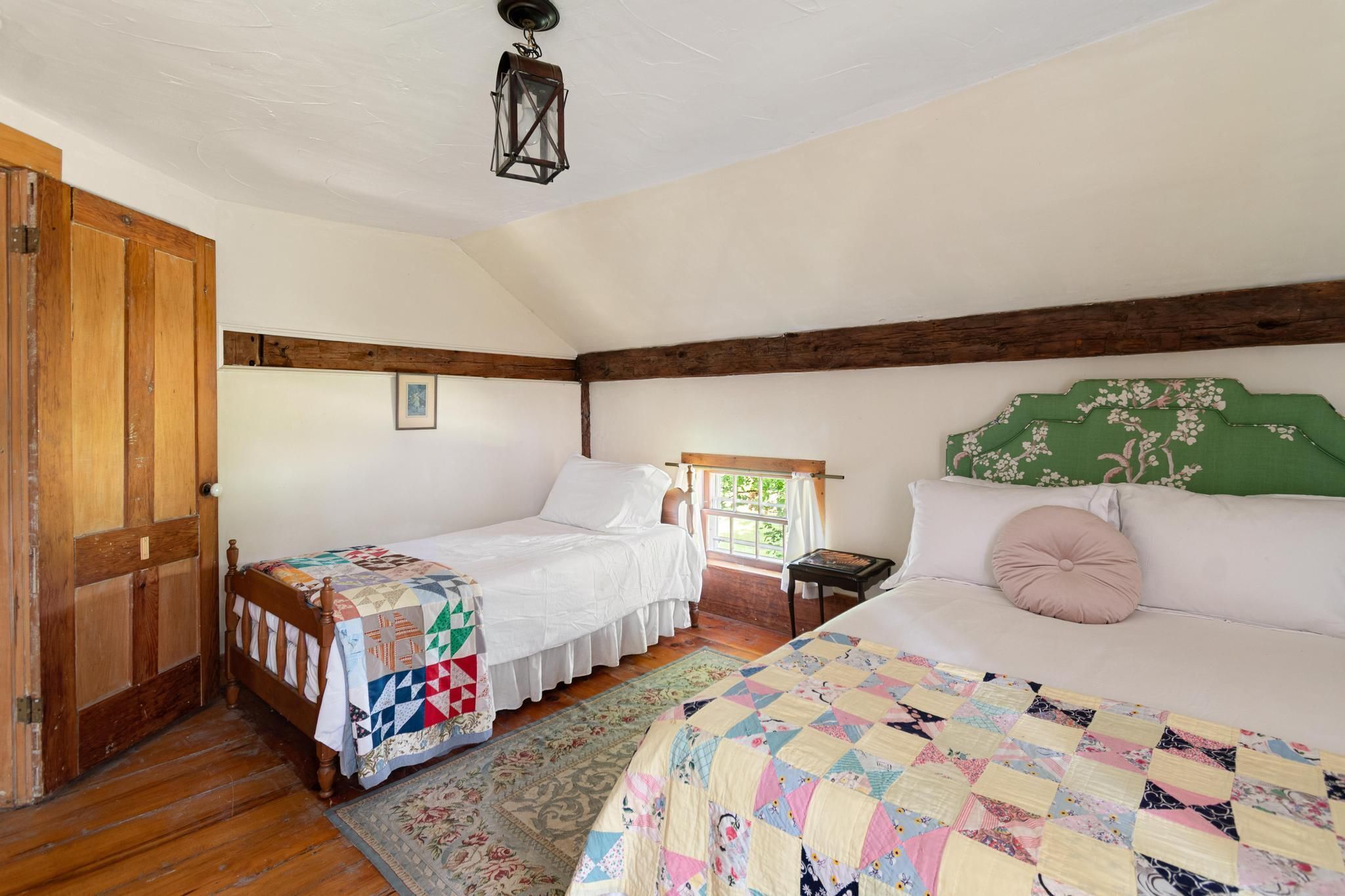 Una camera da letto con due letti, una porta in legno, un quadro appeso al muro e un lampadario.
