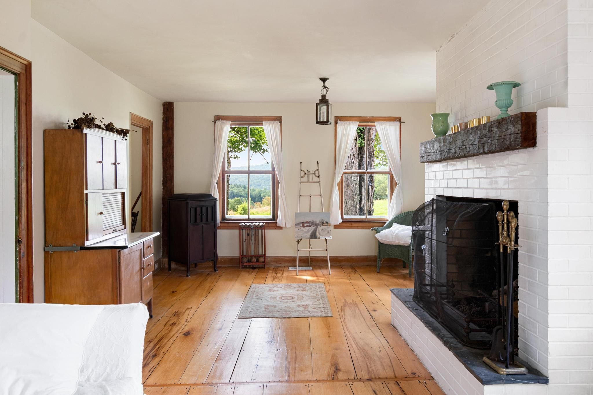 Ein Zimmer mit Kamin, Holzboden und Blick ins Freie durch Fenster.