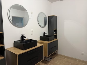 Een moderne badkamer met twee zwarte wasbakken, houten kastjes en ronde spiegels.