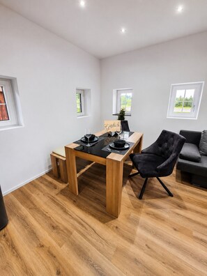 Ein modernes Zimmer mit einem Holztisch, einem schwarzen Stuhl, einem grauen Sofa und einem kleinen Topfpflanzen.