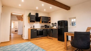 Une cuisine moderne avec des meubles en bois, un réfrigérateur noir et un coin repas comprenant une table et des chaises.