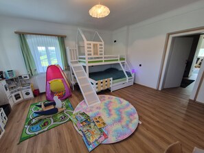 Une chambre d’enfant avec des lits superposés, une tente de jeu, une cuisine miniature et un tapis coloré.