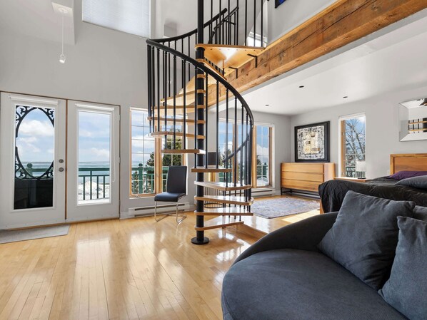 Un intérieur moderne avec un escalier en colimaçon, un balcon offrant une vue dégagée, un canapé et un plafond en bois.