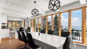Un espace repas moderne doté d’une grande table, de chaises et de larges fenêtres offrant une vue sur la mer.