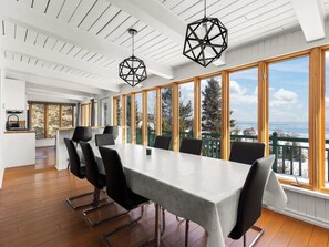 A modern dining area with a large table, black chairs, and large windows offering a view of the sea.