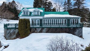 Une grande maison à deux étages, dotée d’un toit végétalisé et de murs blancs, entourée de neige et d’arbres.