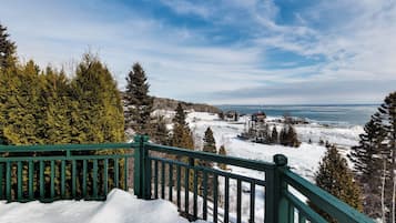 Un paysage enneigé avec une terrasse en bois et une vue sur une ville lointaine et une étendue d’eau.