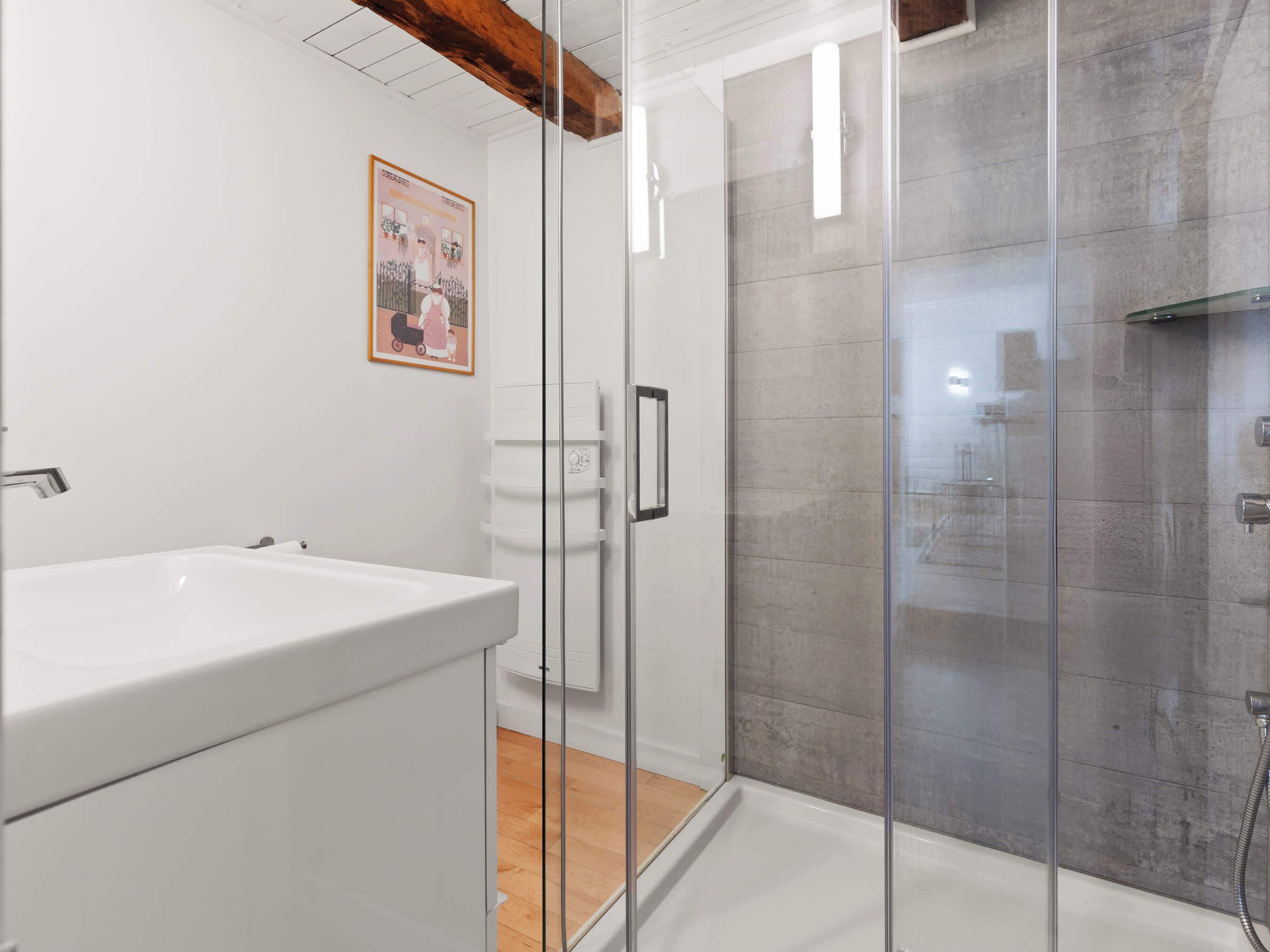 Une salle de bain moderne avec une douche à parois de verre, un lavabo blanc et une poutre en bois au plafond.