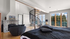 Une chambre spacieuse avec un grand lit, une cheminée, un escalier et une vue sur l’extérieur.